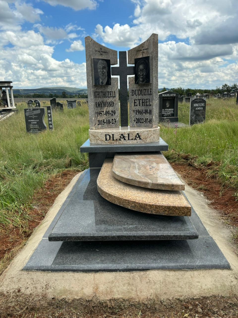 A complete cream and brown granite memorial with a sculpted cross and polished black base